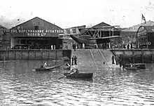 Black-and-white photo of aircraft sheds, facing out onto the sea.