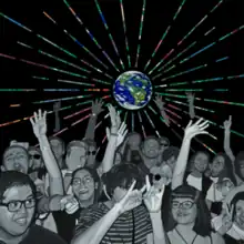 A crowd of people gathered under a globe projecting multi-coloured beams of light