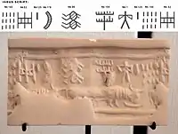 Impression of an Indus cylinder seal discovered in Susa, in strata dated to 2600–1700 BC. Elongated buffalo with line of standard Indus script signs. Tell of the Susa acropolis. Louvre Museum, reference Sb 2425. Indus script numbering convention per Asko Parpola.