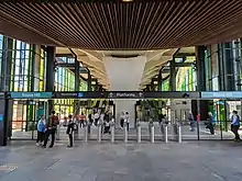 Picture of Rouse Hill station. The station has elevated platforms. The picture was taken below the platforms at the ground level concourse, which is surrounded by green-coloured glass on the exterior.