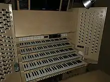 A five-manual modern organ console finished in light coloured wood. About 60 white drawstops are visible on each side, organised in columns by division.