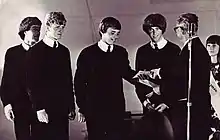 A black-and-white image of four men standing on a stage receiving a prize