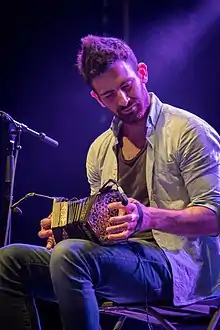 Mohsen Amini plays the concertina, sitting on a stage lit in purple