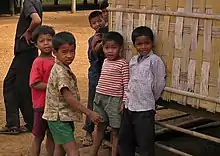 Six young children standing in front of a building with a woven wall