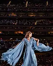 Swift dressed in a white gown, singing into a microphone.