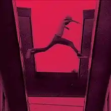 A red-tinted film still showing a boy jumping from one roof to another