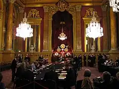 A view of the inside of Goldsmiths' Hall, a long table surrounded by jurors test coins