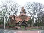 A cruciform church with a central tower with a spire and steeply pitched red tile roofs