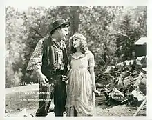 A young woman standing next to a tall strong country-side man.