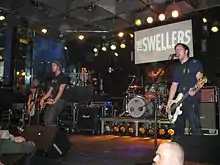 Four men performing onstage playing and singing into microphones