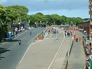 alt=TT 
Grandstand area with scoreboard to extreme left, course start/finish to left (in distance), pit lane with re-fuelling equipment and acceleration lane to centre