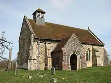 A small stone church with a red tiled roof seen from the southwest, showing a south porch and a small bellcote