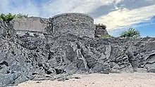 A stone platform, previously the site of a gun battery, located on top of a low cliff and seen from the beach below the cliff.