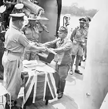 a black and white photograph of a uniformed Japanese officer handing a sword to a uniformed Australian officer