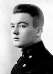 Profile of a young white man with hair thick on top and short at the sides, wearing a dark jacket with two columns of buttons down the chest and an anchor emblem on the side of the upright collar.