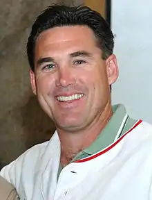 A man in a white baseball jersey over an olive polo