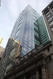 The dark-blue and light-blue patterned glass facade of the building, as seen from 45th Street. The Lyceum Theatre, a short stone building with ornate decoration, is next to 1540 Broadway.