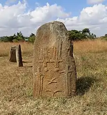 An upright stele with carvings resembling swords. Two stelae in the backgroung.