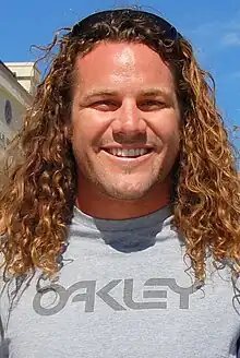 A man wearing black sunglasses on top of his head (to hold back his long hair) and a gray t-shirt.