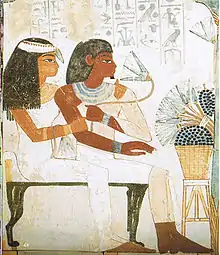 Tawy embracing Nakht as he smells a lotus, whilst they sit together before a set of offerings