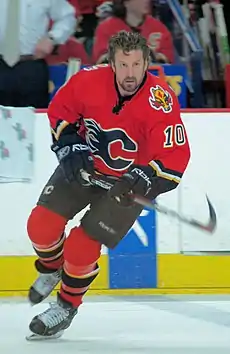 An ice hockey player on the ice skating towards the camera. He is wearing a red and black jersey.