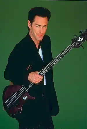 A man with a bass guitar against a green backdrop