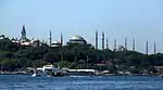 A large building with a square tower, three mosques and ten minarets near water.