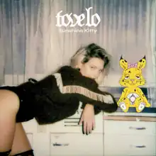 A woman leans over and props herself up with her elbows on the counter, her dark roots visible beneath bleached hair and her upper legs exposed. A yellow cartoon rabbit sits to the right.