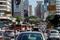 Looking down a busy road, which is banked on both sides by tall buildings, some of which are covered in advertisement billboards (from Transport)