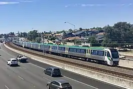 Six car electric multiple unit train running on tracks within the median strip of a freeway