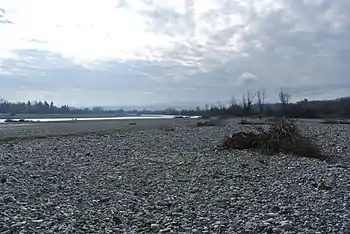 Photo shows a river bordered by an immense bed of white stones. There are mountains in the distance.