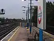 A grey railway station with railway tracks on either side of it, four blue lampposts protruding from the middle of it, and a blue sky above