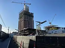 A high-rise building under construction with tall crane along side a light rail station platform