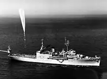 A massive balloon hovers above a naval ship where it is tethered.