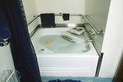 A small bathtub is visible in the center of the image. Bubbles, a rubber ducky, and a small floating boat can be seen in the tub, while two books, a soap bar, and a tooth paste tube can be seen around the rim of the bathtub.