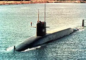 A submarine on the surface with sailors standing on its sail.