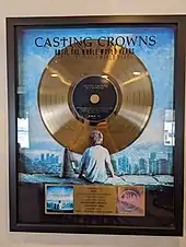 A trophy in the shape of a golden gramophone record is laid into a plaque. The album's artwork is in the background of the award.