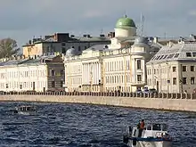 A row of large, stone three-storey buildings alongside a large riverbank