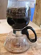 Step 5: At this point, the coffee has been fully brewed, but still contains the coffee grounds. The glass carafe is taken off the heated surface.