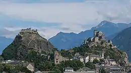 Two hills on which a fortified church lies on the left and a castle on the right. In the background are mountains.