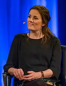 dark-hared white woman sitting, wearing headset microphone, facing right of camera