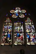 General view of St Peter's stained glass window, with three sections showing a figure with a halo talking to a group of figures.