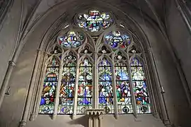 Low-angle view of the Virgin's stained glass window with six sections above with numerous figures and three rosettes above.