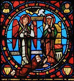 The Annunciation scene in stained glass, from the Saint Denis Basilica (early 12th century). Abbe Suger himself, the builder of the church, is pictured at the feet of the Virgin Mary, at right. She wears red with a green cloak.