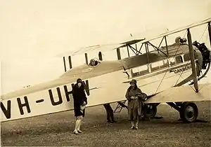 Two women standing in front of large biplane with man in flying gear seated in open cockpit