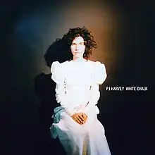 A woman sitting in an upright position in a white Victorian era dress. To her left, white text reads "PJ Harvey White Chalk."