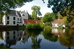 White castle in the middle of a pond with some other building on the side