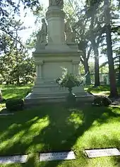 Large stone monument with two women facing opposite directions and another figure cut off at top, in a green cemetery. Of the three visible graves, T. B. Walker is at center and Harriet Hulet Walker is at right