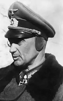 An older man wearing a peaked cap and military coat.