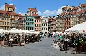 Market square, colourful houses in the background, tourists in restaurants in front